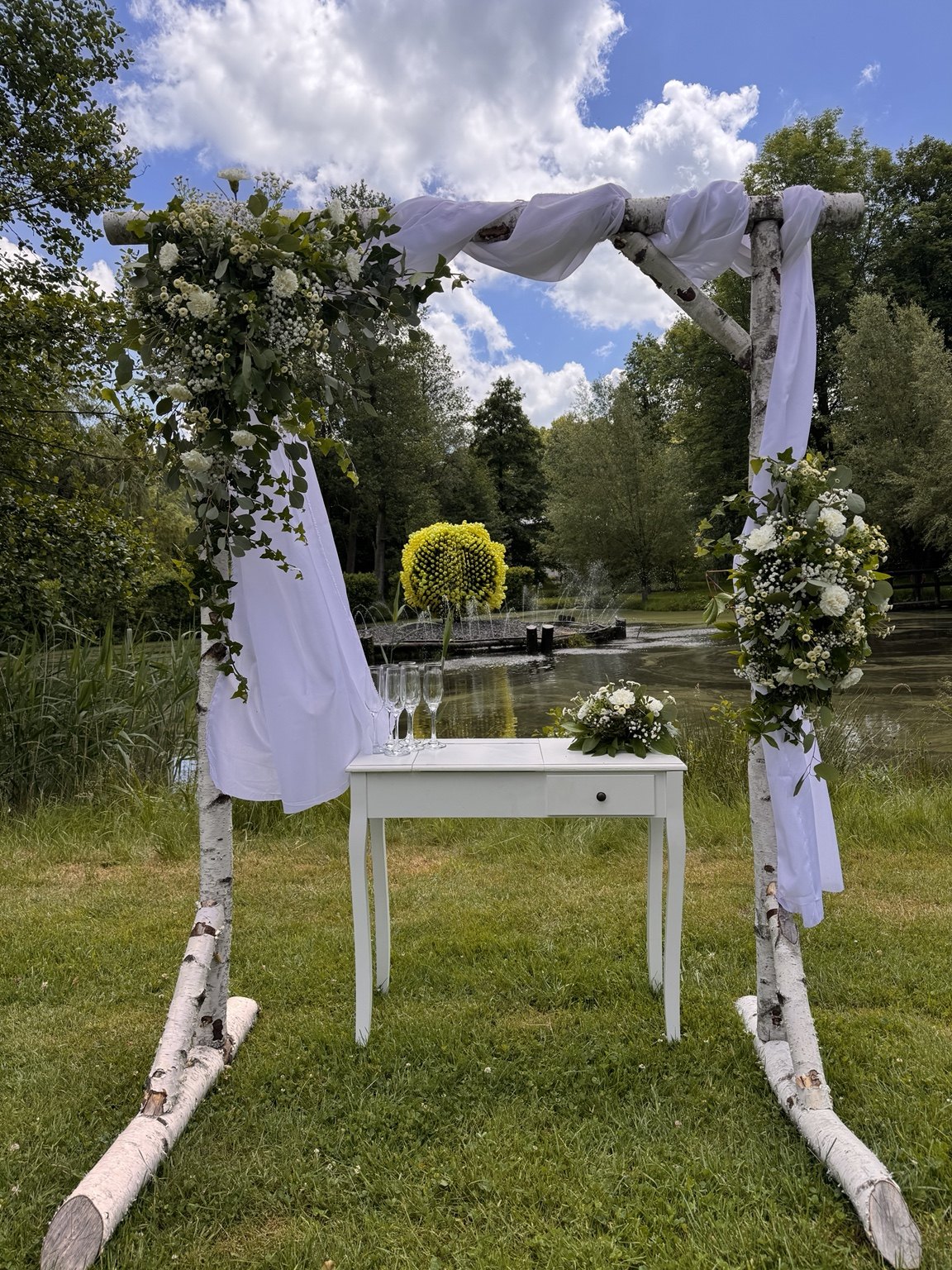 Obřadní oblouk s květinami a bílým stolkem venku na trávě